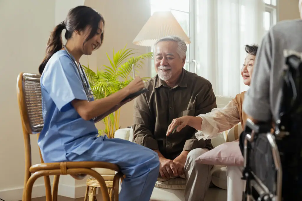 happiness cheerful elderly woman men talking with female caregiver nurse doctor having health checking consult living areacaretakers with senior couple sitting living room nursing home 1